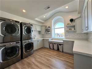 Clothes washing area featuring light hardwood / wood-style flooring, stacked washer and clothes dryer, sink, cabinets, and a textured ceiling