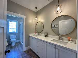 Bathroom with dual sinks, oversized vanity, walk in shower, toilet, and hardwood / wood-style flooring