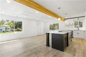Kitchen with light wood-type flooring, a center island, stainless steel electric range, and white cabinetry
