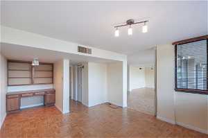 Spare room with built in desk, light parquet flooring, and track lighting