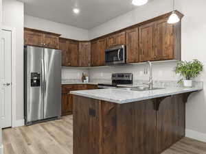 Kitchen featuring sink, kitchen peninsula, pendant lighting, light hardwood / wood-style floors, and appliances with stainless steel finishes