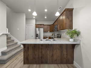 Kitchen with light wood-type flooring, kitchen peninsula, and appliances with stainless steel finishes