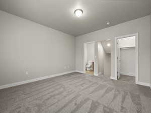 Unfurnished bedroom featuring light carpet, a textured ceiling, a spacious closet, connected bathroom, and a closet