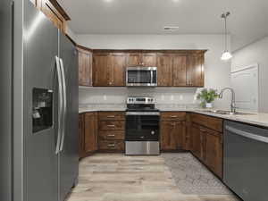 Kitchen featuring sink, hanging light fixtures, stainless steel appliances, light stone counters, and light wood-type flooring