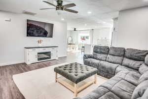 Living room with ceiling fan, light wood-type flooring, and a textured ceiling