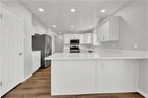 Kitchen with kitchen peninsula, stainless steel appliances, light hardwood / wood-style floors, and white cabinetry