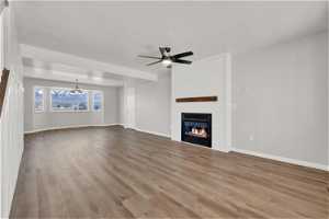 Unfurnished living room featuring ceiling fan with notable chandelier, hardwood / wood-style floors, and a large fireplace