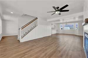 Unfurnished main floor family room with ceiling fan with notable chandelier and light wood-type flooring