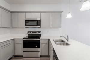 Kitchen featuring hardwood / wood-style flooring, stainless steel appliances, sink, gray cabinets, and decorative light fixtures