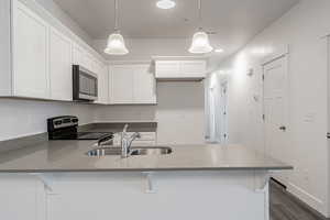 Kitchen featuring white cabinets, sink, electric range, and decorative light fixtures