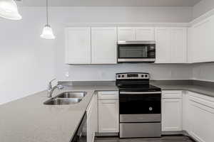 Kitchen with sink, appliances with stainless steel finishes, pendant lighting, and white cabinets