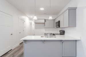 Kitchen with kitchen peninsula, stainless steel appliances, sink, pendant lighting, and light hardwood / wood-style floors