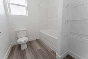 Bathroom with toilet, bathtub / shower combination, and wood-type flooring