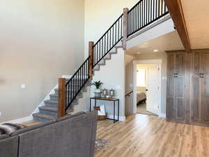 Stairs with beamed ceiling, a towering ceiling, and light wood-type flooring