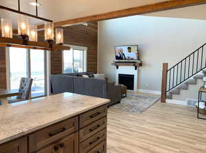 Kitchen featuring beamed ceiling, light stone counters, light hardwood / wood-style flooring, hanging light fixtures, and wood walls