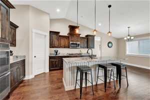 Kitchen with appliances with stainless steel finishes, a breakfast bar, decorative light fixtures, dark hardwood floors, and a center island with sink