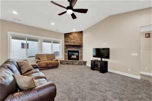 Family room with vaulted ceiling, carpet floors, ceiling fan, and a stone fireplace