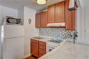 Kitchen with backsplash, white appliances, dark hardwood / wood-style floors, light stone counters, and sink