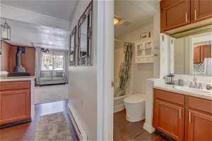 Full bathroom featuring shower / bath combo, toilet, vanity, wood-type flooring, and a baseboard radiator