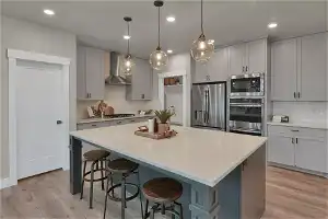 Kitchen featuring wall chimney range hood, light wood-type flooring, backsplash, stainless steel appliances, and a kitchen breakfast bar