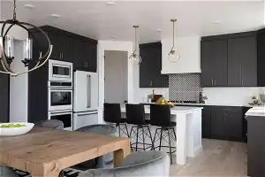 Kitchen with appliances with stainless steel finishes, a center island, backsplash, decorative light fixtures, and light hardwood / wood-style flooring