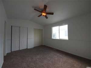 Upstairs bedroom featuring dark colored carpet, ceiling fan, two closets, and lofted ceiling