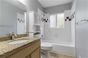 Full bathroom with tiled shower / bath, toilet, tile flooring, and vanity