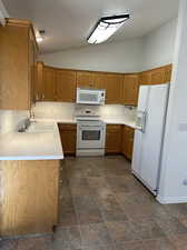 Kitchen with lofted ceiling, white appliances, and sink