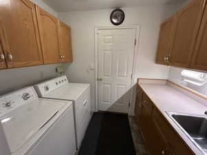 Laundry area featuring separate washer and dryer, cabinets, and sink