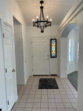 Foyer entrance with an inviting chandelier, a textured ceiling, and light tile patterned floors