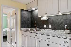 Kitchen featuring white cabinets, light tile floors, sink, and light stone countertops