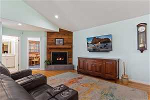 Living room featuring lofted ceiling, a large fireplace, hardwood / wood-style floors, wood walls, and sink