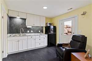 Kitchen with black fridge, white cabinets, dark tile flooring, and tasteful backsplash