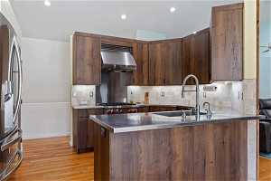 Kitchen with backsplash, light hardwood / wood-style flooring, sink, wall chimney exhaust hood, and stainless steel fridge