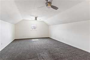 Additional living space with ceiling fan, a textured ceiling, vaulted ceiling, and dark carpet