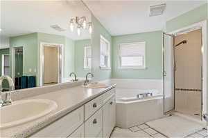 Bathroom with dual sinks, vanity with extensive cabinet space, tile flooring, and shower with separate bathtub