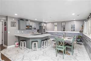 Kitchen with tiled floors, tasteful backsplash, gray cabinets, kitchen bar and stainless steel refrigerator,