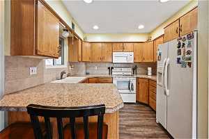 Kitchen with white appliances, dark hardwood / wood-style flooring, sink, and a breakfast bar