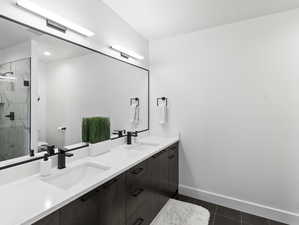 Bathroom with oversized vanity, a shower with shower door, tile floors, and double sink