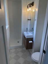 Bathroom featuring vanity, toilet, a tile shower, and tile patterned flooring
