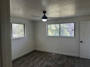 Unfurnished room with dark colored carpet, a textured ceiling, and ceiling fan