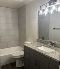 Full bathroom with tiled shower / bath, a textured ceiling, toilet, vanity, and wood-type flooring