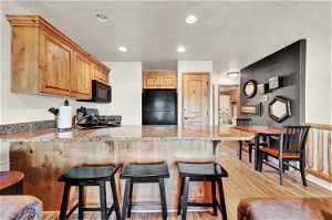 Kitchen with a breakfast bar, light wood-type flooring, black appliances, kitchen peninsula, and light stone counters
