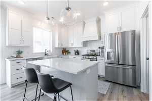 Kitchen with light hardwood / wood-style floors, appliances with stainless steel finishes, backsplash, and custom range hood
