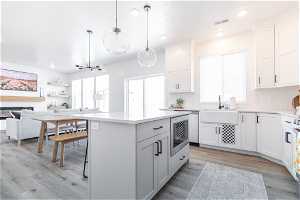 Kitchen with white cabinets, sink, backsplash, hanging light fixtures, and light hardwood / wood-style flooring