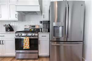 Kitchen featuring appliances with stainless steel finishes, light wood-type flooring, backsplash, and white cabinetry