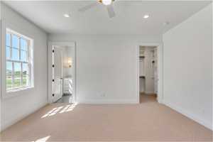Unfurnished bedroom featuring light colored carpet, ceiling fan, a spacious closet, and ensuite bathroom