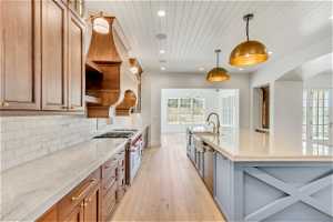 Kitchen featuring light stone countertops, backsplash, double oven range, pendant lighting, and light wood-type flooring