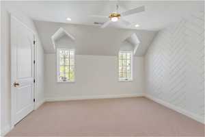Additional living space with a healthy amount of sunlight, ceiling fan, vaulted ceiling, and light carpet