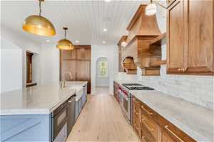 Kitchen with hanging light fixtures, range with two ovens, light hardwood / wood-style flooring, backsplash, and a center island with sink
